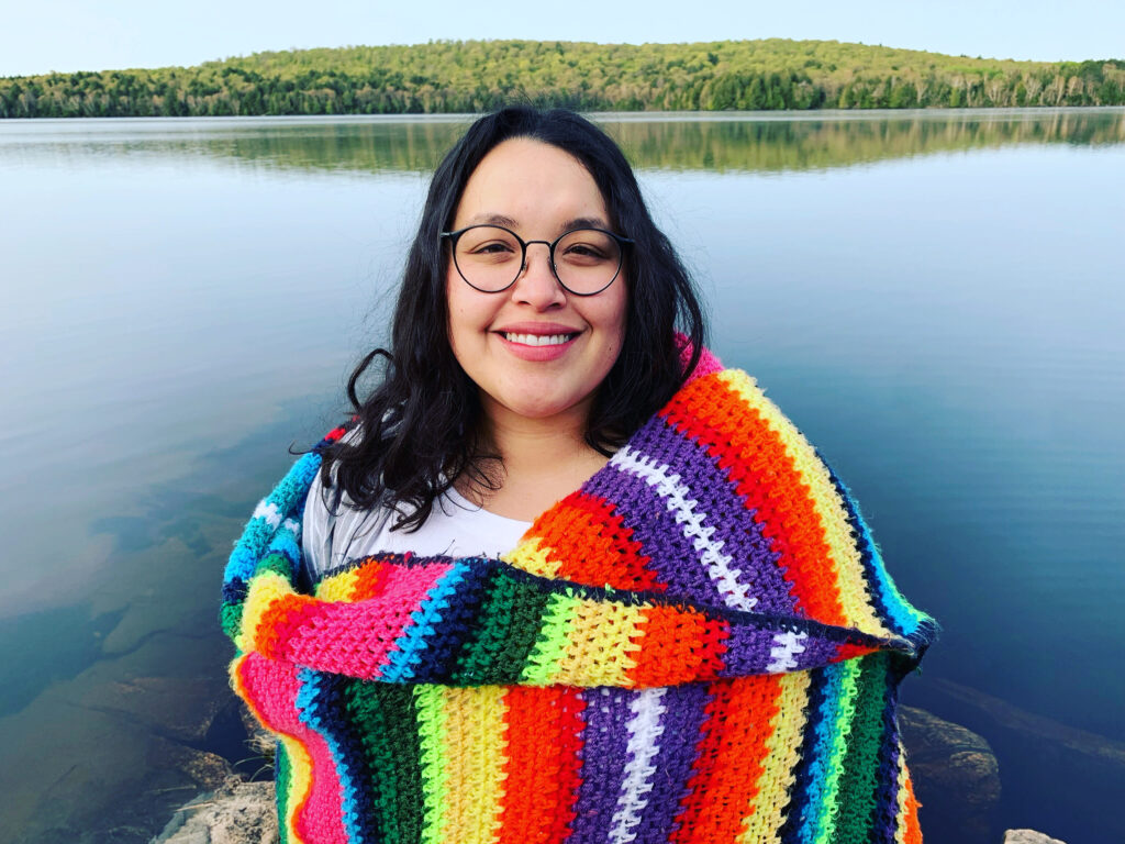 Isishaj wrapped up in a Latin colourful blanket, stading on a rock on Hay Lake, South Algonquin, ON